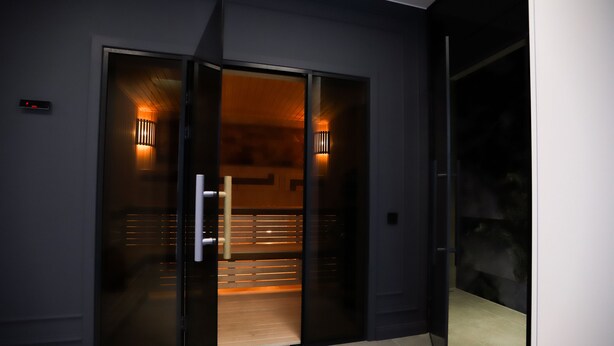 Une entrée d’hôtel moderne avec une porte en verre, un écran numérique et un éclairage intérieur chaleureux.