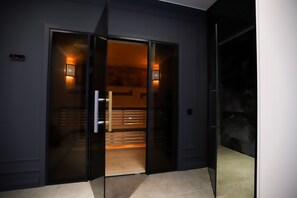 Une entrée d’hôtel moderne avec une porte en verre, un écran numérique et un éclairage intérieur chaleureux.