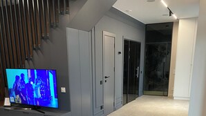 Un salon moderne avec un téléviseur, des meubles de rangement gris, une table en bois et deux poufs marron.
