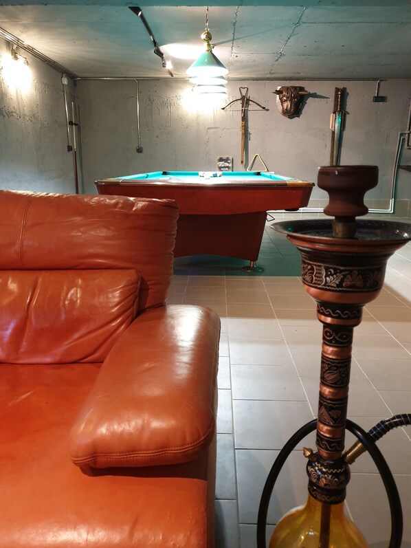 Une pièce avec une table de billard, un canapé en cuir et un narguilé.