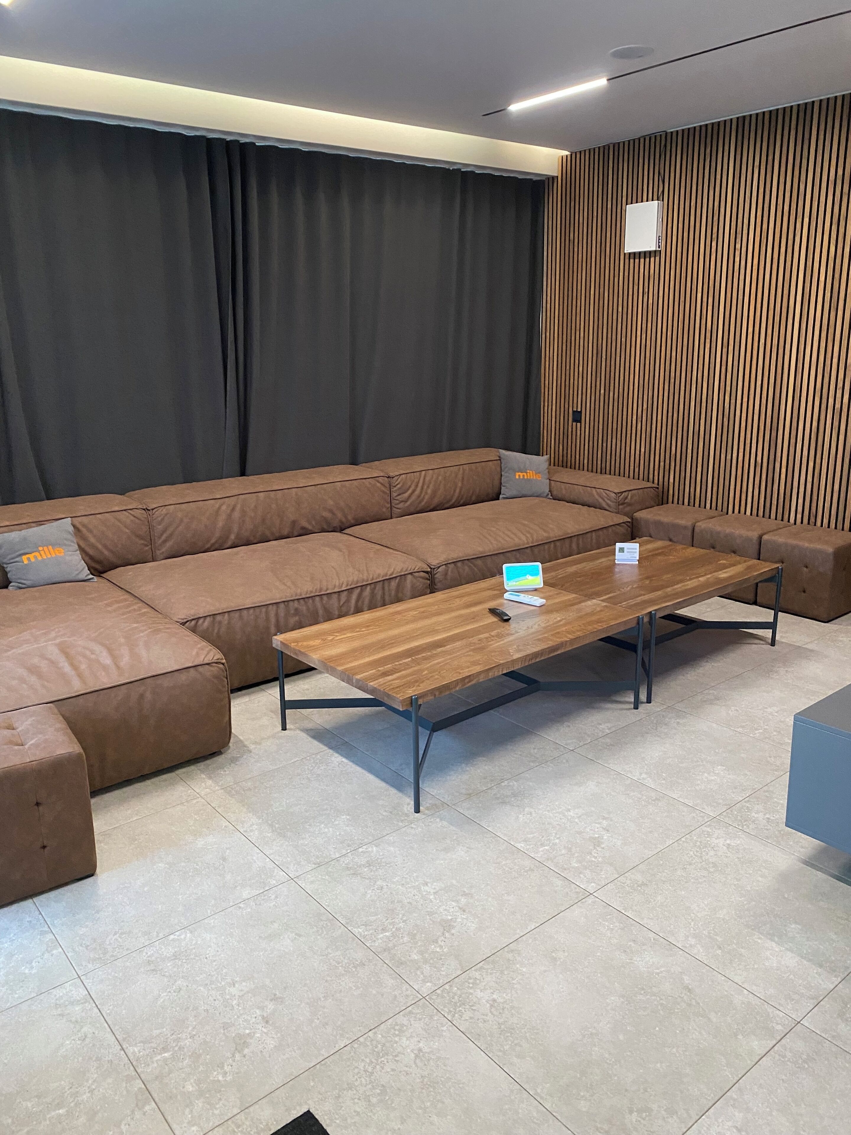 Un soggiorno moderno con un divano componibile marrone, un tavolino in legno e una tenda nera.