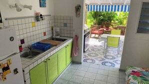 Ett kompakt kök med gröna skåp, kakel ovanför arbetsbänken och en liten matplats med ett bord och stolar.