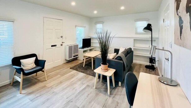 Ein geräumiges Wohnzimmer mit einer Couch, einem Sessel, einem kleinen Tisch mit Pflanze, einem Fernseher und einer Lampe.