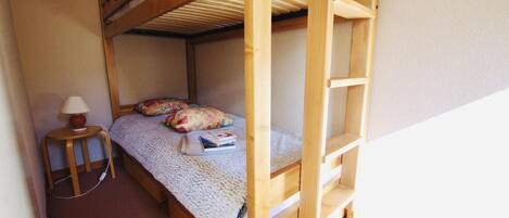 A bunk bed room with a small bedside table, a lamp, and a few pillows.