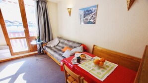 Ett mysigt rum med en soffa, ett matbord med en röd duk och ett fönster med utsikt över bergen.