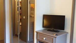 Ett hotellrum med en tv på en byrå, en garderob med hyllor och en dörr som leder till ett annat rum.