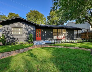 Stunning two-story home with a unique architectural style, featuring a charming red front door and a well-manicured lawn.