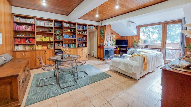 A spacious living area with a large bookshelf, a dining table with chairs, a sofa, and a television. - La Mansardina (Roma)