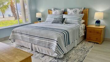 Un dormitorio con una cama grande, dos mesitas de noche con lámparas, una mesita auxiliar de madera, una alfombra estampada y una ventana con persianas.