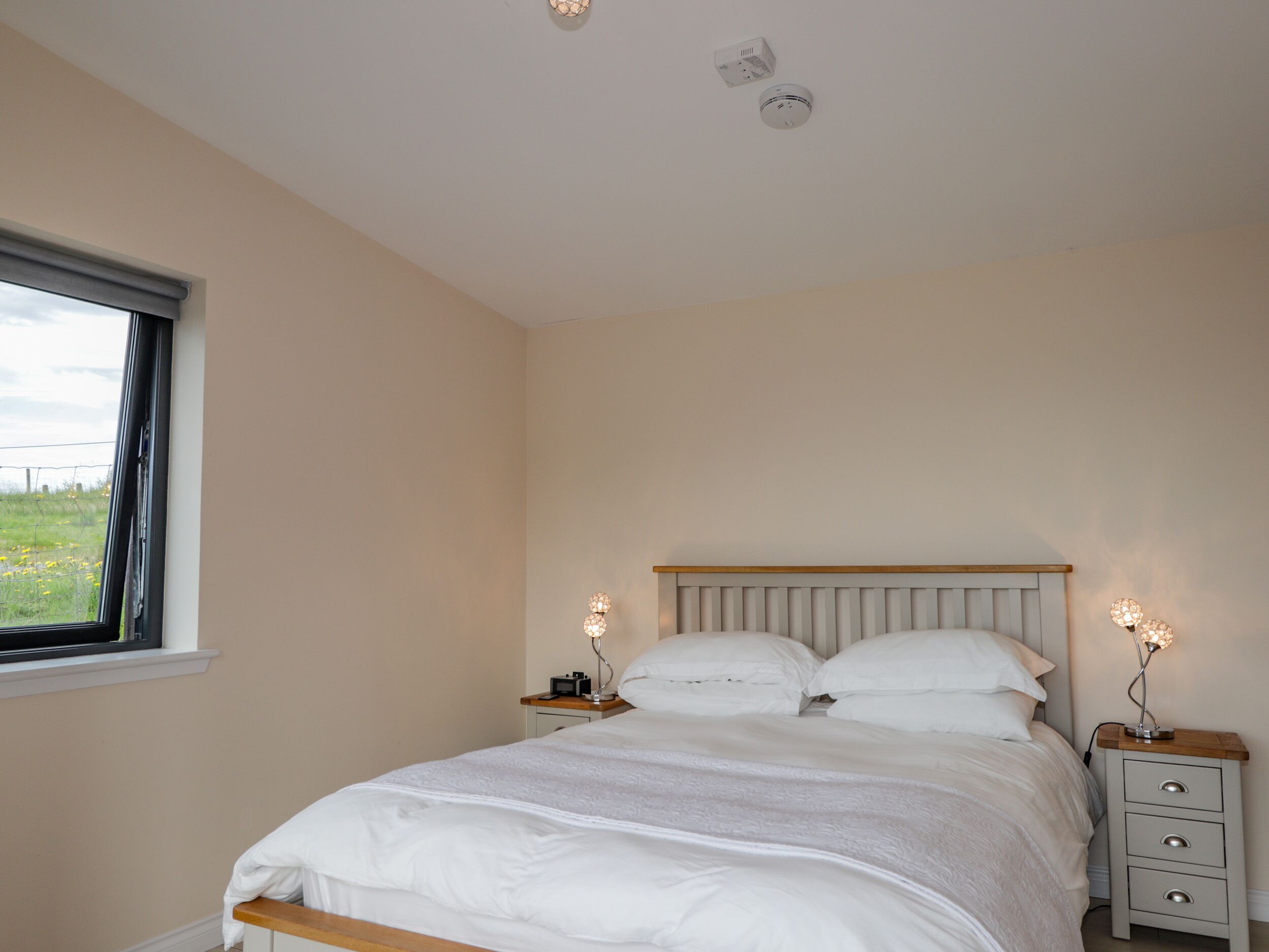 Een slaapkamer met een bed, nachtkastjes, een raam en een plafondlamp.