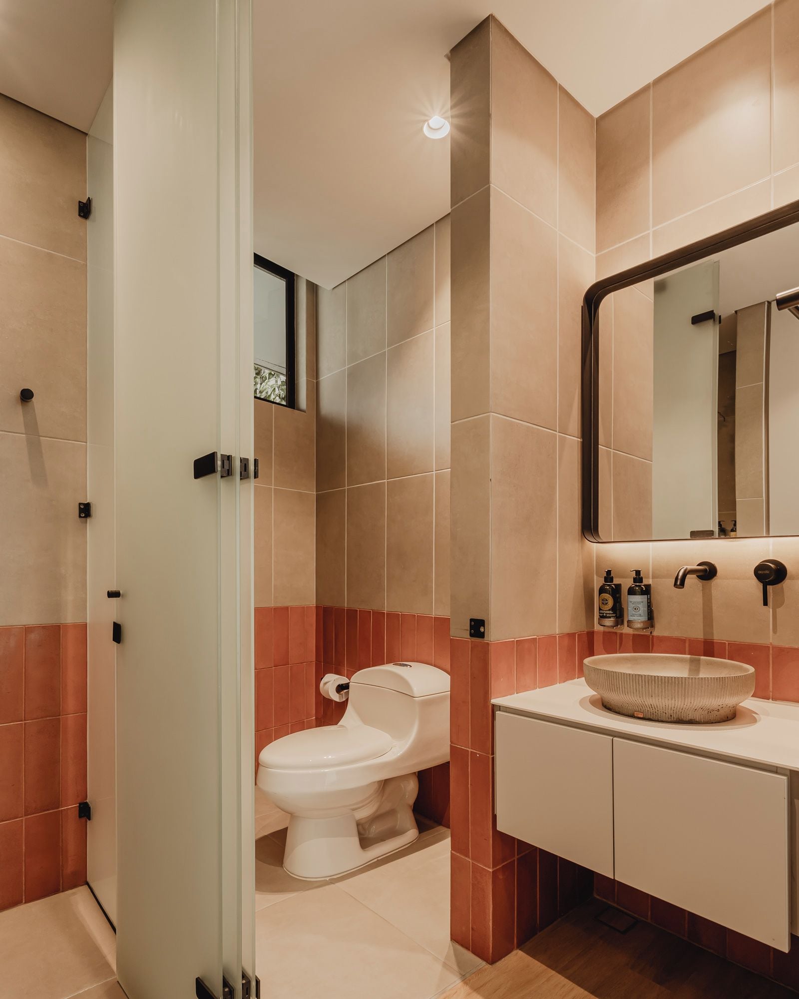 Egy modern fürőszoba, amelyben WC, mosdókagyló és tükör található.