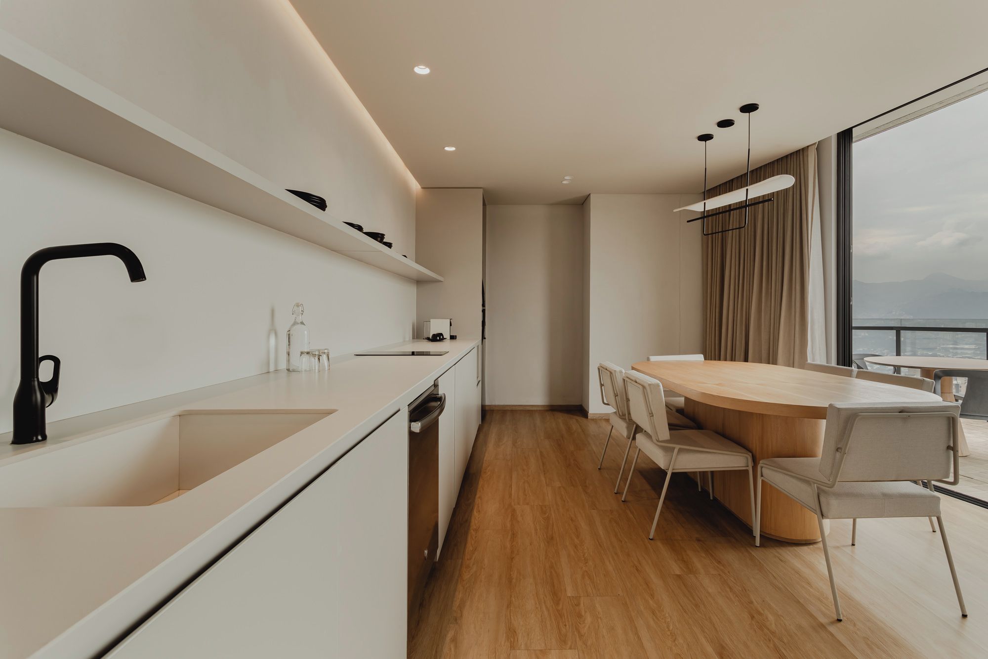 Una cocina moderna con horno integrado, un comedor con mesa redonda y sillas, y vistas de la ciudad a través de amplias ventanas.
