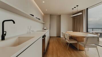 Una cocina moderna con horno integrado, un comedor con mesa redonda y sillas, y vistas de la ciudad a través de amplias ventanas.
