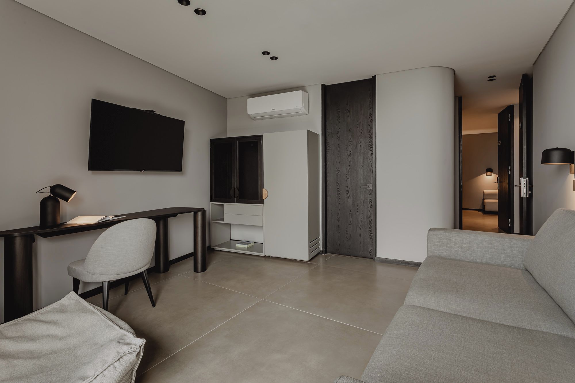 Una sala de estar moderna con una televisión de pantalla plana, un escritorio con lámpara, un sofá gris y un armario.