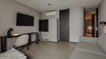 Una sala de estar moderna con una televisión de pantalla plana, un escritorio con lámpara, un sofá gris y un armario.
