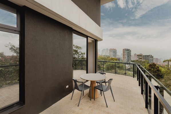 A modern balcony with a round table and chairs, large windows, and a city view. - Feeling Residences (Medellín)