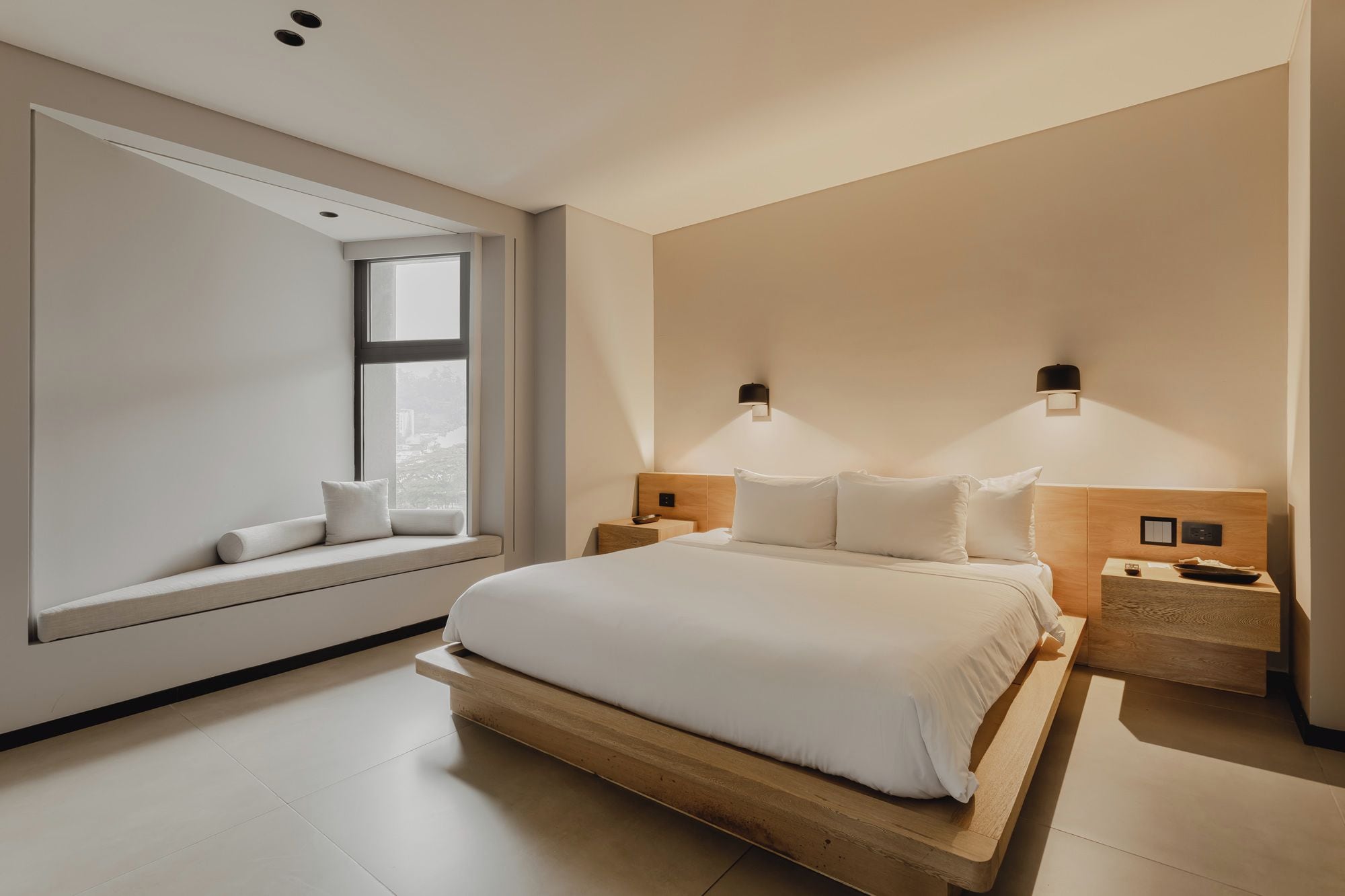 A modern bedroom with a large bed, built-in nightstands, and a window seat.