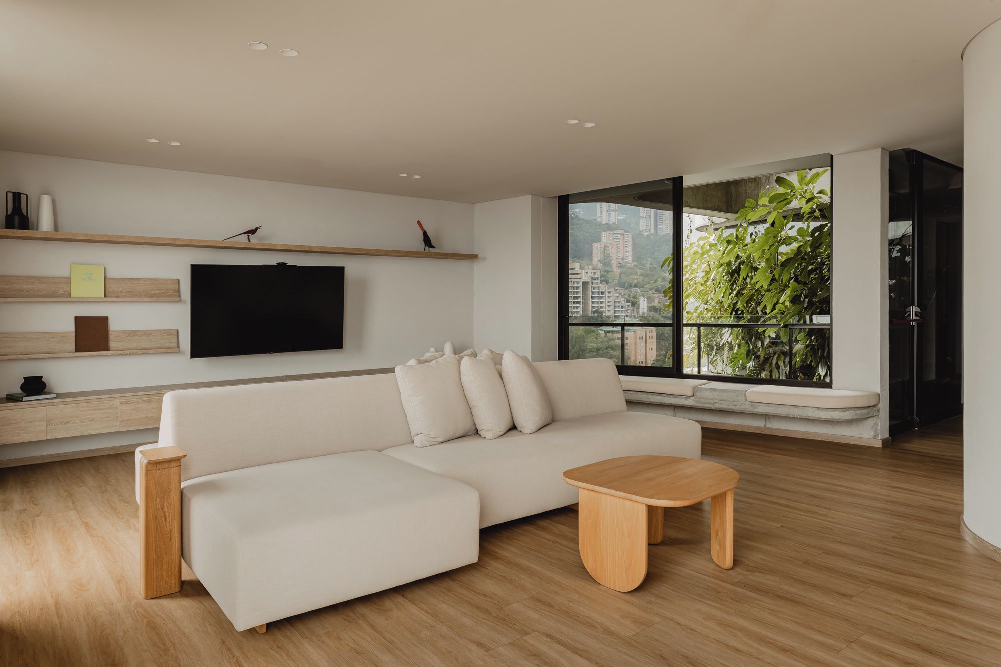 A modern living room with a white sofa, wooden coffee table, and a TV mounted on the wall.