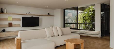 A modern living room with a white sofa, wooden coffee table, and a TV mounted on the wall.