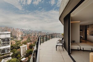Un balcón con vistas a la ciudad, una zona de estar con sofá y sillones, y una decoración interior moderna.