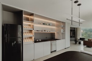 Una cocina moderna con muebles blancos, estantes empotrados, un refrigerador negro y un comedor con mesa y sillas.