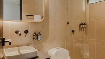 A modern bathroom with a large mirror, a sink, a toilet, and a shower area.