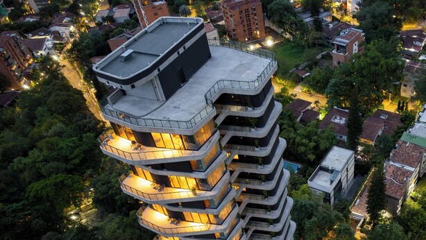 Un edificio a più piani con balconi, immerso nel verde e circondato da altri edifici.