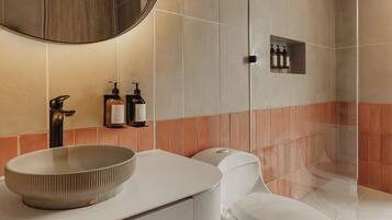A modern bathroom with a round sink, a toilet, and a shower area.
