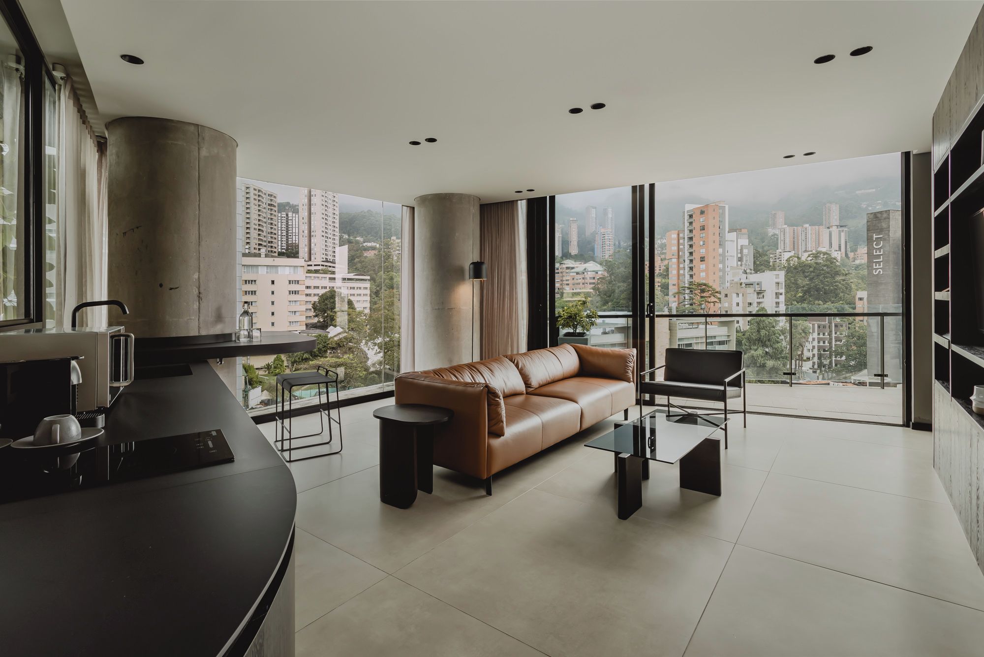 A modern living room with a sofa, a coffee table, and a view of a cityscape through large windows.