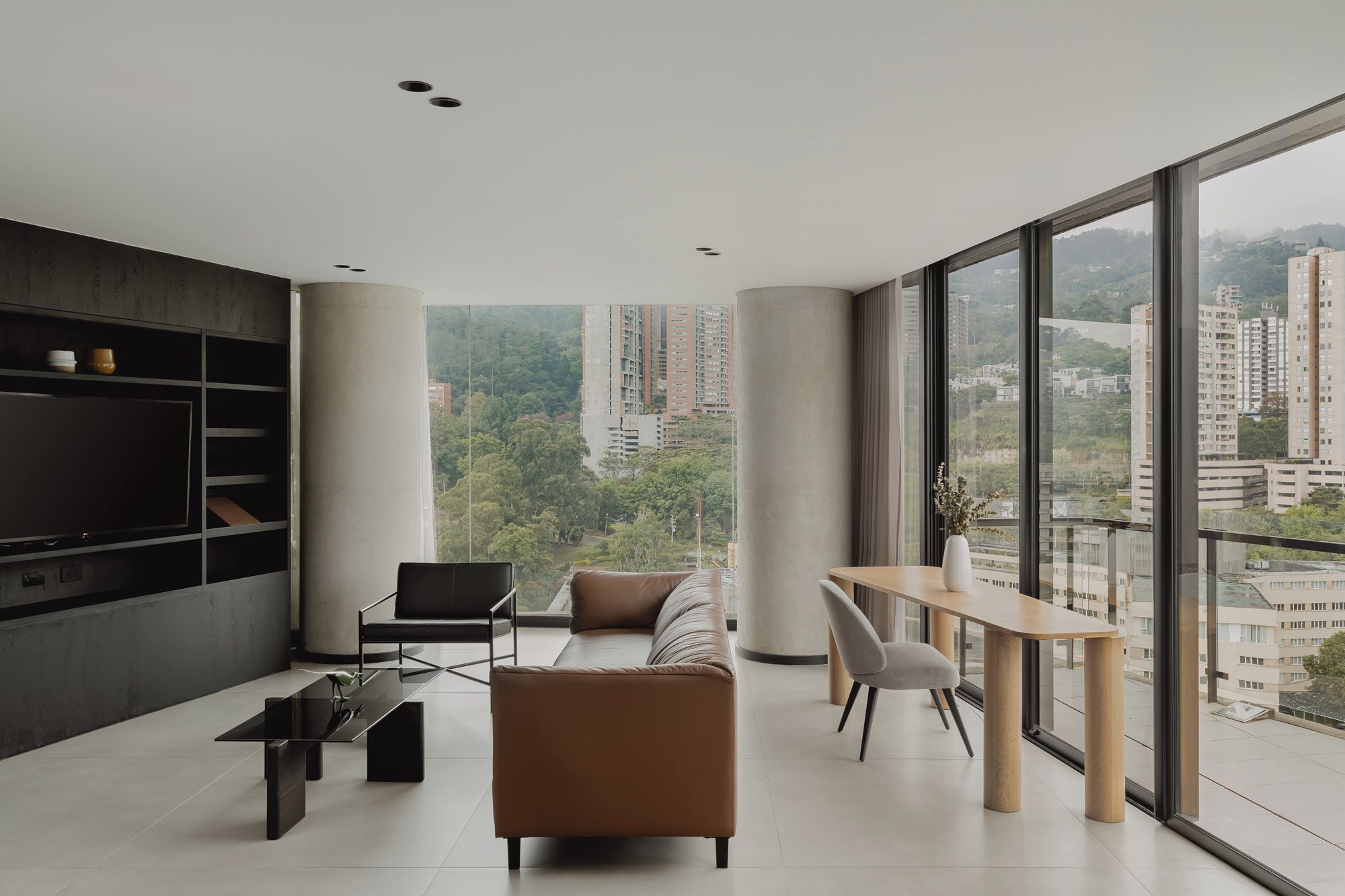 A modern living room with a large TV, comfortable seating, and a dining area with a view of the city.