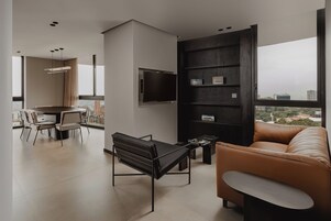 Una sala de estar moderna con un sofá, una mesa de centro, un televisor montado en la pared y un comedor con sillas y una mesa.