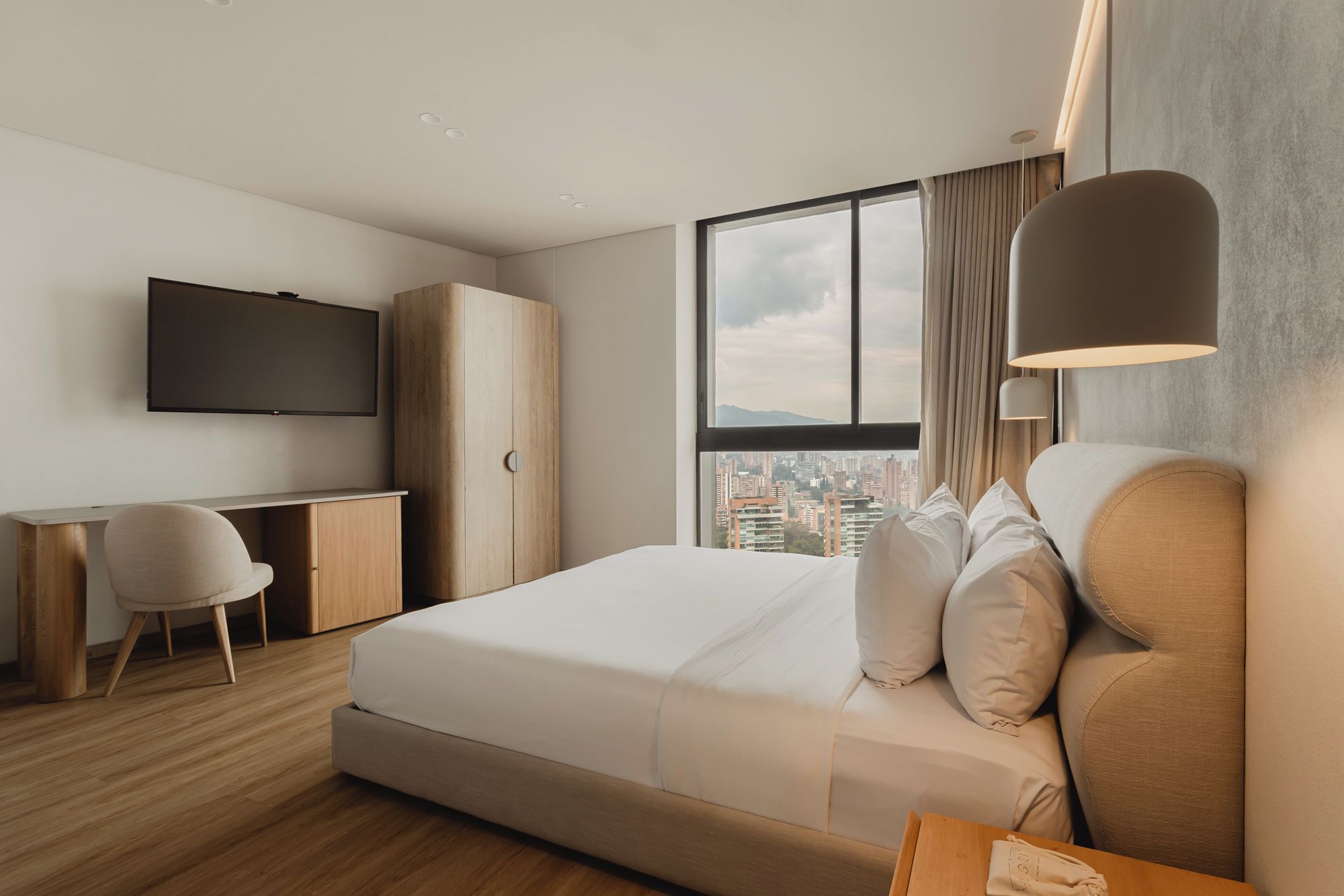 A modern hotel room with a bed, a desk, a chair, and a TV.
