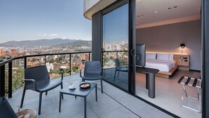 Una camera d'hotel moderna con balcone, un letto, una TV e un angolo ristoro con sedie e tavolo.