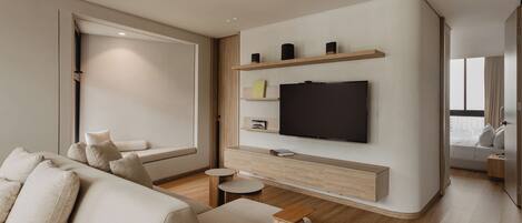 A modern living room with a sofa, a flat-screen TV mounted on a wooden wall, a small round table, and a window with a view.