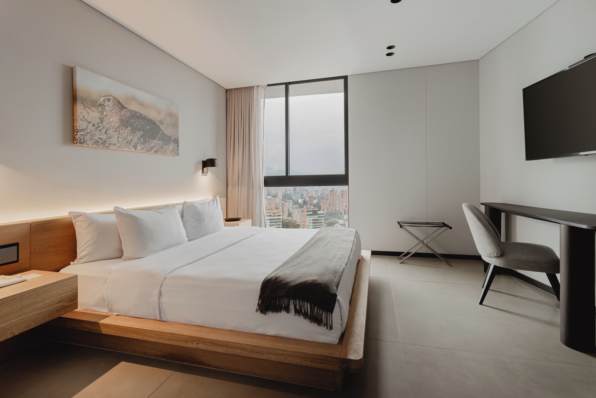 Een moderne hotelkamer met een groot bed, een bureau en uitzicht over de stad.