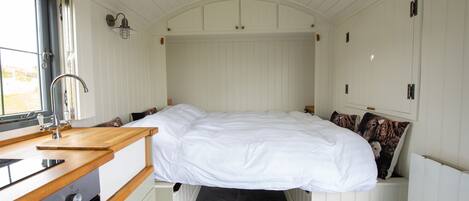 A compact, well-lit room with a bed, a small kitchenette, and a window providing natural light.