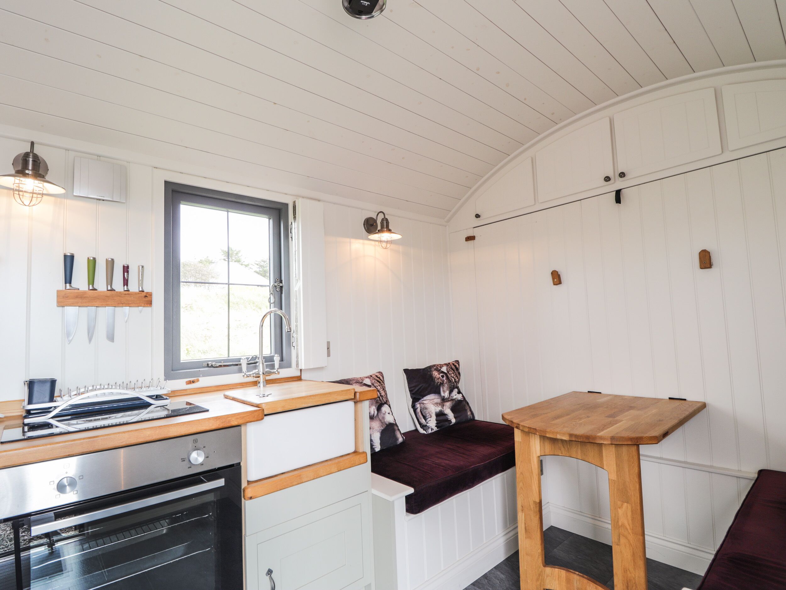 Una cocina con paredes de madera blanca, una ventana, un lavamanos, una estufa y una mesa de madera.