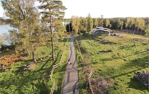 A rural landscape with a paved path, a building with a sloped roof, and a body of water in the background.