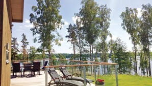 En udendørs terrasse med et bord og stole, der giver udsigt over en sø med træer i baggrunden.