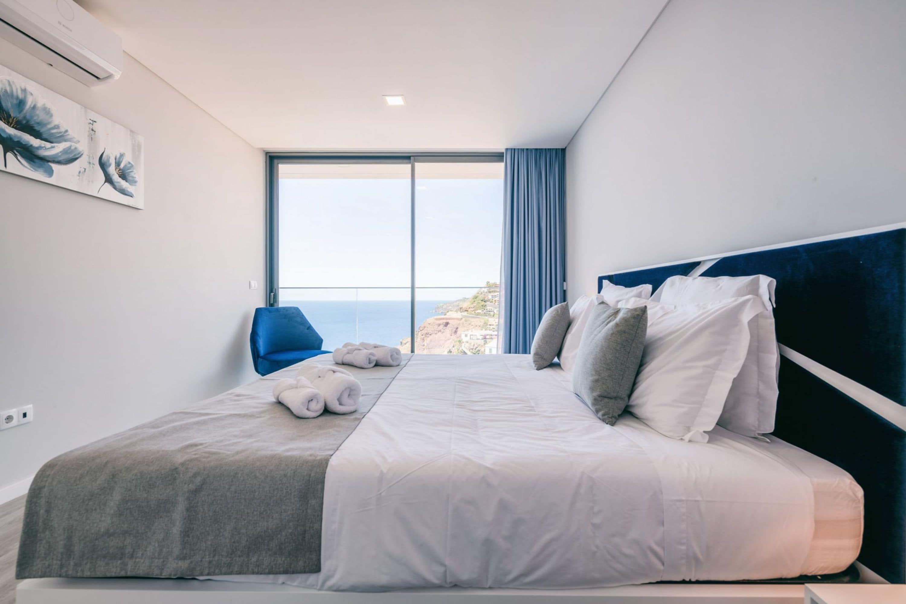 Ett hotellrum med en stor säng, utsikt över havet och en blå stol.