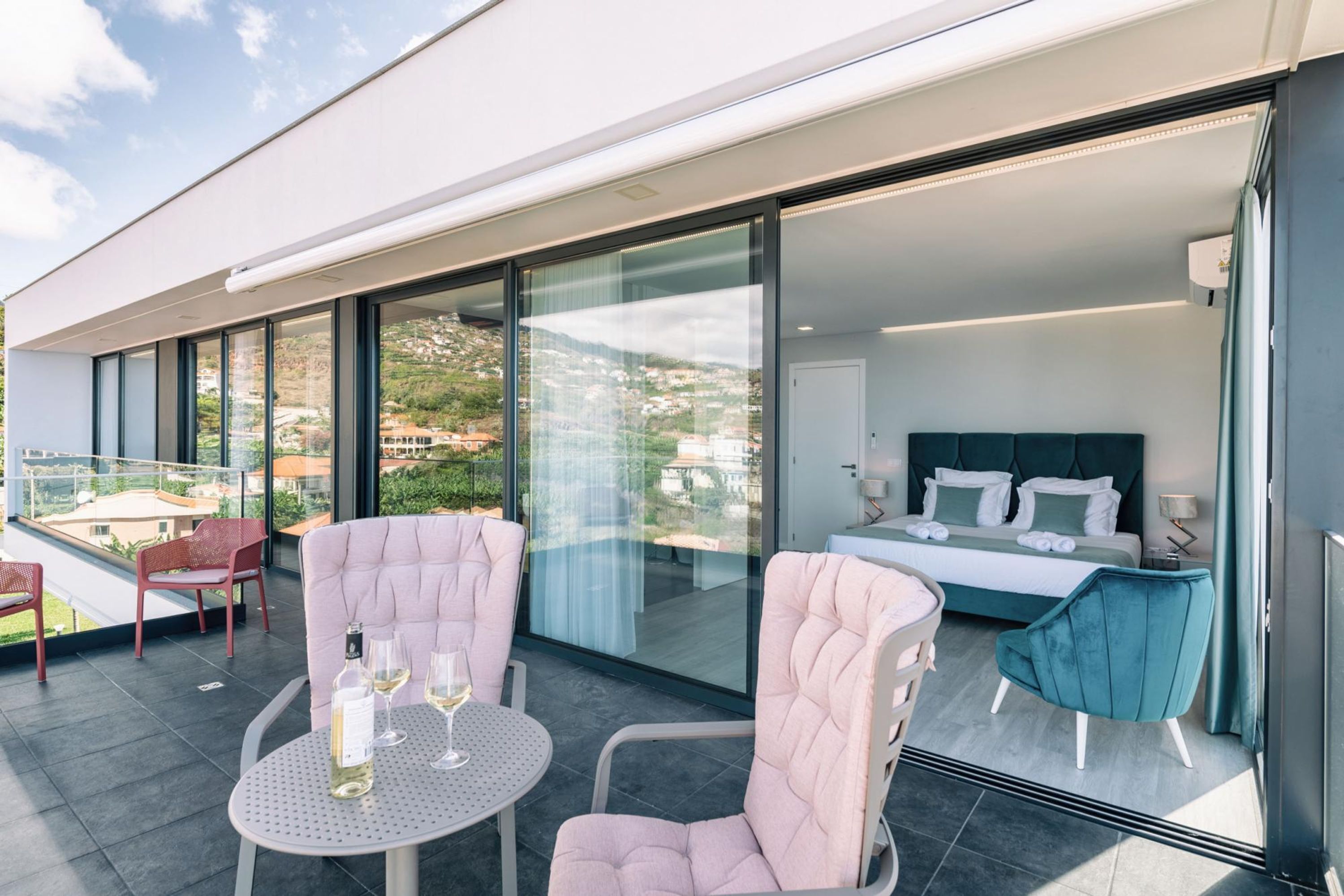 Een moderne hotelkamer met een groot bed, een balkon met zitplaatsen en uitzicht op de omgeving.