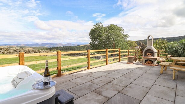Eine Terrasse mit Whirlpool, Gartenmöbeln und einem Steinofen.