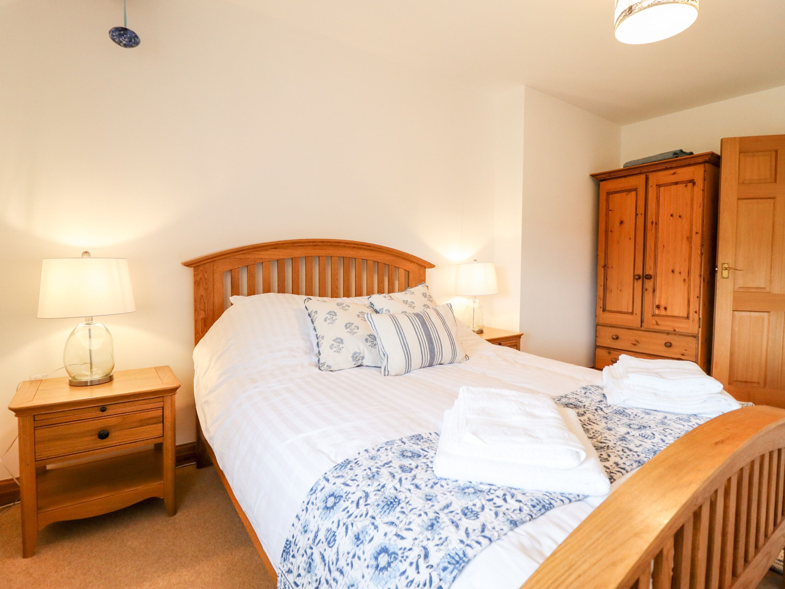 A neatly made bed with a wooden headboard, two bedside tables with lamps, and a wooden wardrobe.