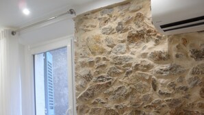 Ein Zimmer mit einer Steinwand, einem Fenster mit Jalousien und einem schwarzen Heizkörper.