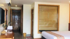 A hotel room with a wooden floor, a bed with a white and orange bedspread, a wooden desk with a chair, a small plant, and a window with blinds. - Lien Minh Hostel & Homestay-  Family Balcony Room With Mountain View (Sa Pa)