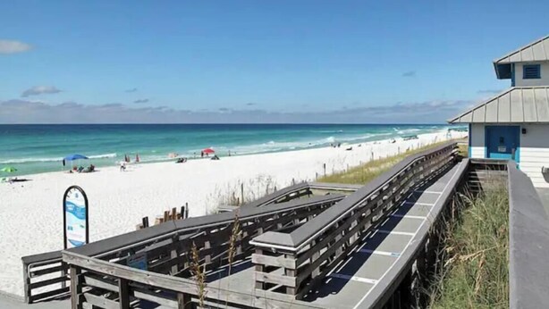 Ein Strand mit einer Holzpromenade, die zu einem Gebäude mit einer blauen Tür führt.