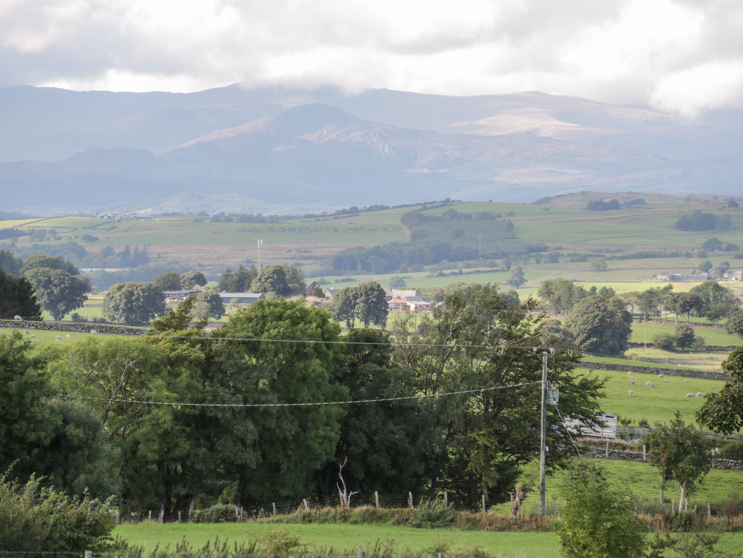A rural landscape with rolling hills, scattered trees, and a few buildings in the distance.