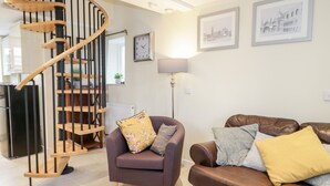 Un salon moderne avec un escalier en colimaçon en bois, un fauteuil violet, un canapé en cuir marron et deux tableaux encadrés accrochés au mur.