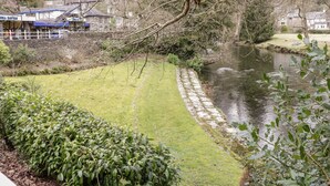 Une vue sur la rivière, avec un sentier en pierre, des espaces verts et des bâtiments en arrière-plan.