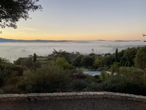 Un paysage comprenant un mur de pierre, une végétation luxuriante et une vue lointaine d’une vallée enveloppée de brume.